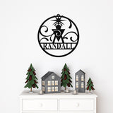 May include: Black metal Christmas ornament with the name "Randall" in a circular design. The ornament features a star and decorative swirls. Below, a white dresser displays miniature Christmas trees and houses.