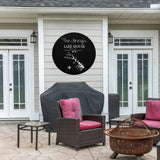 May include: Black metal sign with white text that reads "The Jenny's Lake House Established 2017 Lake Sonoma, VA". The sign features a stylized lake outline with a compass and crossed oars. The sign is mounted on a light gray wooden wall outside a home with a patio set.