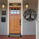 May include: Black metal tree of life wall art with the name "FISHER" displayed on a rectangular plaque. The tree design features a circular frame with leaves and branches. The artwork is mounted on a gray exterior wall.